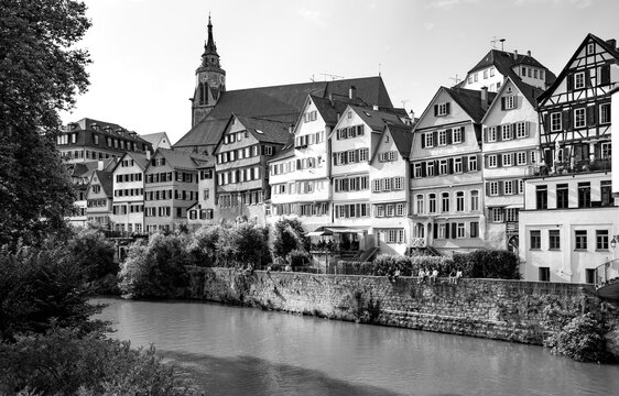Black and white view from Eberhardsbr&uuml;cke across the Neckar River to T&uuml;bingen&rsquo;s historic waterfront with traditional houses and the Collegiate Church.