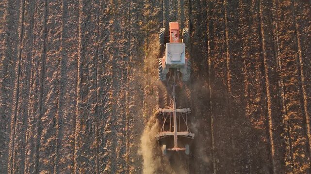 Top-down view of a tractor with cultivator tilling a field at golden hour