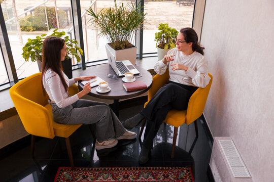 Two elegant young Caucasian women plan marketing content while sipping coffee. Concept of strategic communication and modern digital business. Top view
