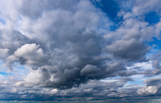 Powerful dark storm clouds mixed with bright cumulus formations and patches of blue sky create a dramatic and atmospheric natural cloudscape.