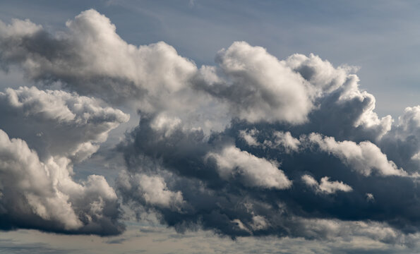 Large sculptural storm clouds illuminated by sunlight create a dramatic atmospheric sky with strong contrasts between bright cloud edges and dark formations.