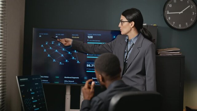Caucasian young adult woman presenting cybersecurity network screen to African American young adult engineer. Clip suitable for corporate software security training and enterprise tech promotions