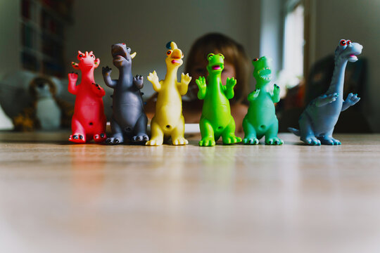 Colorful toy dinosaurs stand in a row on a wooden table with a blurred child in the background. Creative child development concept highlighting imaginative play and authentic domestic atmosphere.