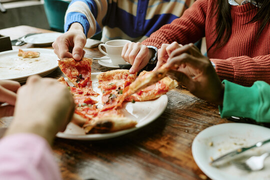 Multiethnic young adult friends sharing pizza slices together in cafe, close up shot. Concept represents dining, friendship, food delivery advertising and lifestyle marketing