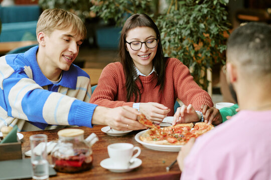 Diverse multiethnic group of young adult friends sharing pizza while sitting in cafe. Image suitable for restaurant marketing, food service promotion and social leisure campaigns