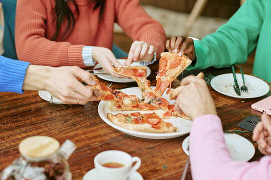 Multiethnic young adult friends taking pizza slices from plate during lunch meeting in cafe. Image suitable for restaurant marketing and food delivery advertising