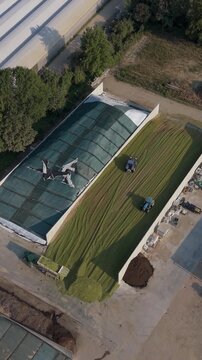 Drone view of agricultural tractors loading freshly cut grass into a silage pit and spreading and compacting the forage for storage in Lombardy, Italy.