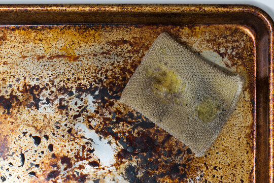 Dirty stained cookie sheet aluminum baking pan bakeware with old cleaning sponge.