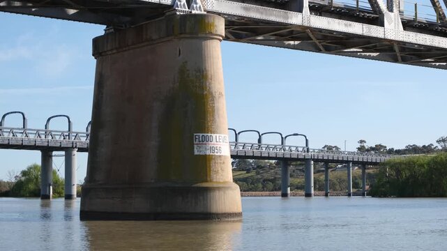Stone pylon supporting the historic railway bridge in Murray Bridge, South Australia, featuring the marked flood level sign with the adjacent road bridge visible across the Murray River&nbsp;