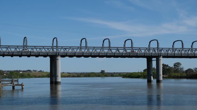 Vehicles driving across the historic road bridge over the calm Murray River in Murray Bridge, South Australia, with pedestrians crossing the adjacent cantilevered walkway