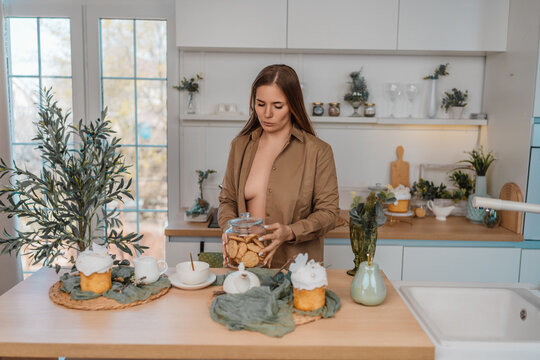 Brunette woman retrieving homemade biscuits from glass jar in bright modern kitchen