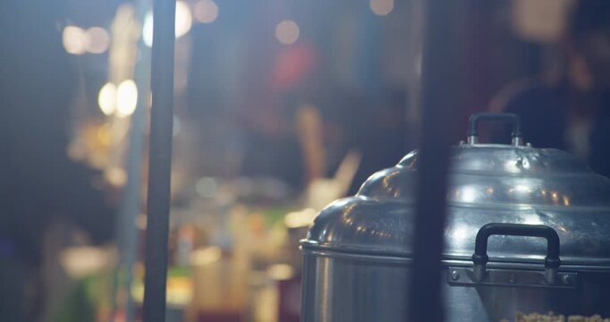 Stacked steel steamer pots glow under warm light at a Thai night market stall selling steamed buns and dumplings.
