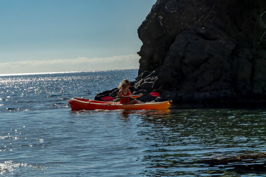 Kayaking, ocean, woman enjoying an active summer vacation on blue sparkling water near a rock