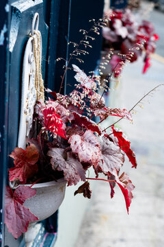 Beautiful autumn style red leaves in a vintage white wall mounted flowerpot decorating a dark blue exterior wall with a softly blurred outdoor background