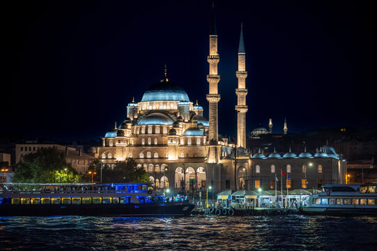 Istanbul,turkey,august 4, 2025. Yeni cami illuminated at night on the bosphorus, ottoman mosque with domes and minarets reflecting on water amid boats and ferries