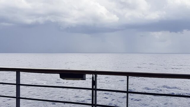 Overcast stormy sky with heavy thunderclouds over a calm open sea, filmed from a ship deck with railing in the Mediterranean. Static tripod shot, 4K.