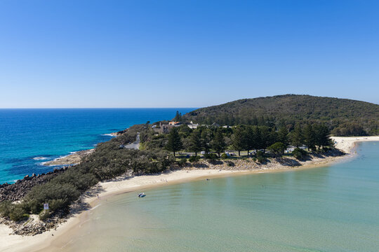An aerial view of Laggers Point surrounded by clear turquoise ocean, with the historic Trial Bay Gaol visible in the background. 