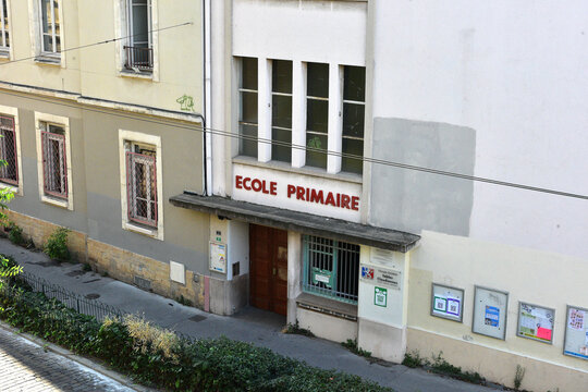 Historic French primary school facade with 'Ecole Primaire' sign on a sloped cobblestone street, Lyon, France