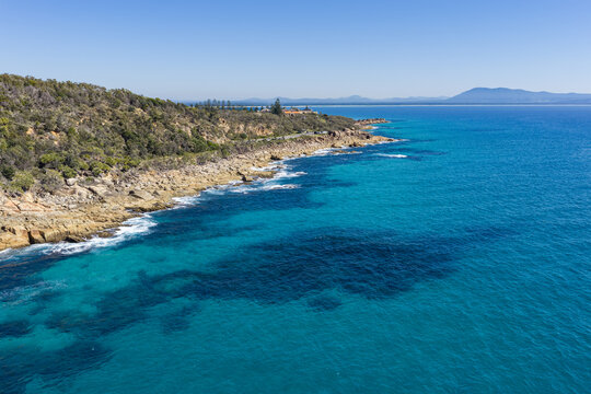 Aerial view of the rugged rocky coastline at Monument Hill in Trial Bay, surrounded by clear turquoise water near South West Rocks, New South Wales, Australia.