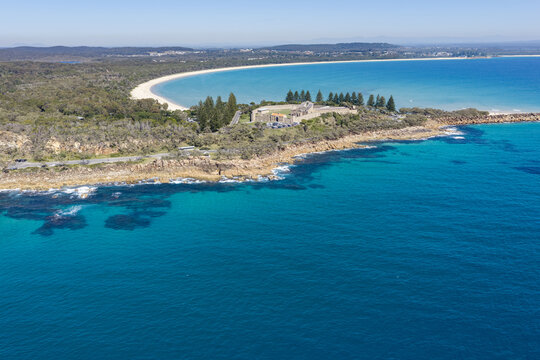 Aerial view of the rugged rocky coastline at Monument Hill, with the historic Trial Bay Gaol overlooking the turquoise ocean near South West Rocks, New South Wales, Australia.