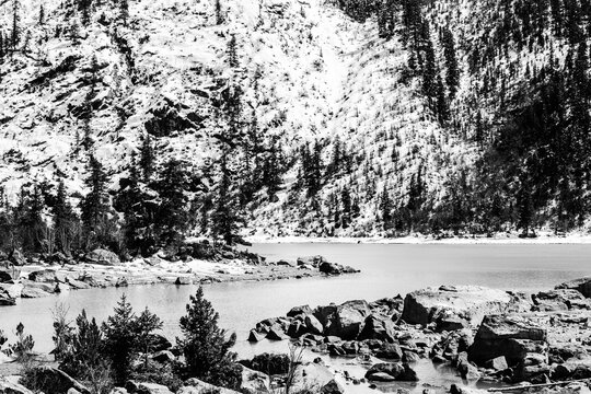 Snowy forest beside a frozen alpine lake in black and white