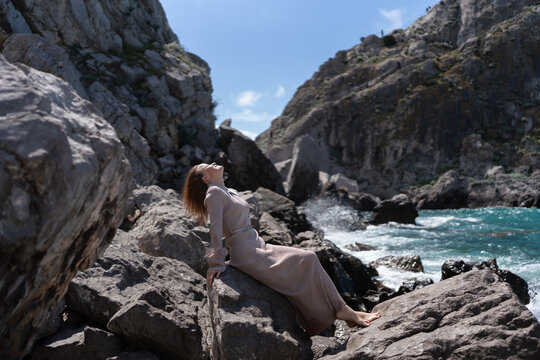 Young woman sitting on rocks near sea while enjoying sunny weather in a beautiful coastal landscape