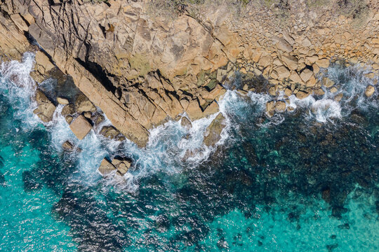 Downward aerial view of powerful ocean waves crashing onto the rugged rocky coastline at Trial Bay near South West Rocks, New South Wales, Australia.