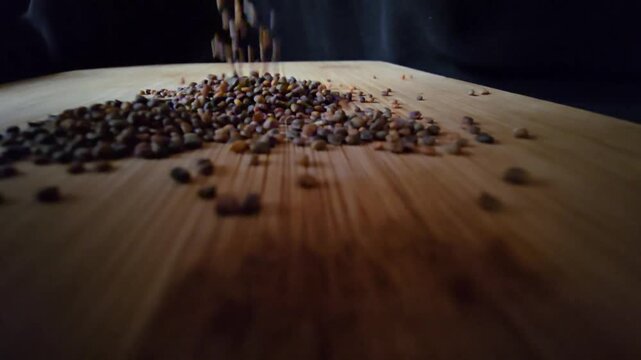 Macro shot of organic arugula and rocket seeds pouring and falling onto a wooden surface, creating a dynamic motion for agricultural and food themes.   