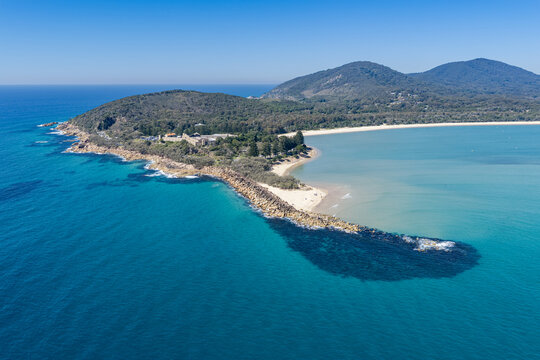 Aerial view over Laggers Point and Front Beach, surrounded by clear turquoise waters and backed by forested mountains at South West Rocks, New South Wales, Australia.