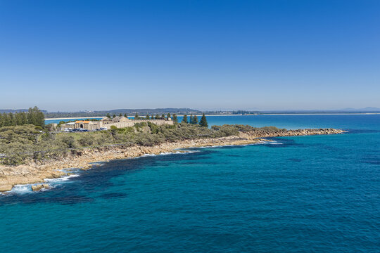 Aerial view of Laggers Point featuring the historic Trial Bay Gaol, rugged coastline, turquoise ocean and forested mountains near South West Rocks, New South Wales, Australia.