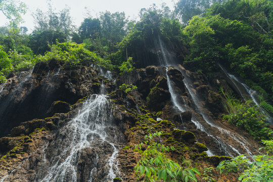 Waterfalls cascading down dark rocky cliffs covered in lush tropical foliage in Java Indonesia