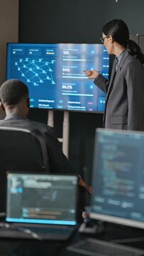 Vertical video of Caucasian young adult woman presenting cybersecurity data on monitor to African American colleague. Ideal for corporate cybersecurity and technology training content