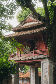 Khue Van Cac pavilion with round wooden window and tiled roof framed by green tree branches at Temple of Literature in Hanoi Vietnam