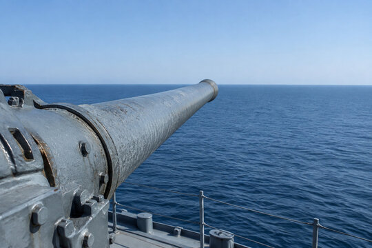 Close-up of a historic naval gun barrel pointing towards an empty ocean horizon.