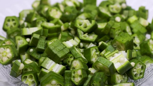 Fresh chopped okra pieces rotating on glass plate against white background in slow motion.