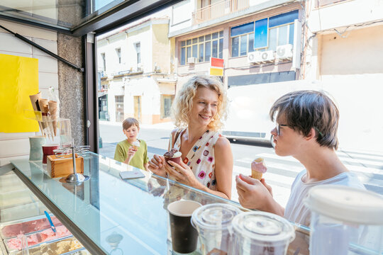 Happy mother and two sons enjoying fresh gelato together during summer day in Spain