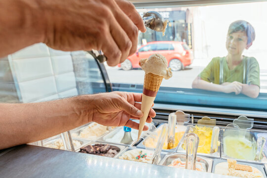 Curious young boy watching fresh gelato cone being prepared at local ice cream shop