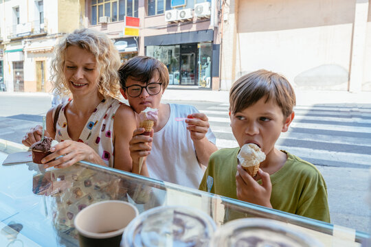 Cheerful family eating gelato together outside local ice cream shop on summer vacation
