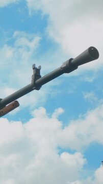 A detailed low angle shot of a rifle barrel and front sight post pointing towards a bright sky with white clouds. Suitable for historical documentaries or war reenactment themes.