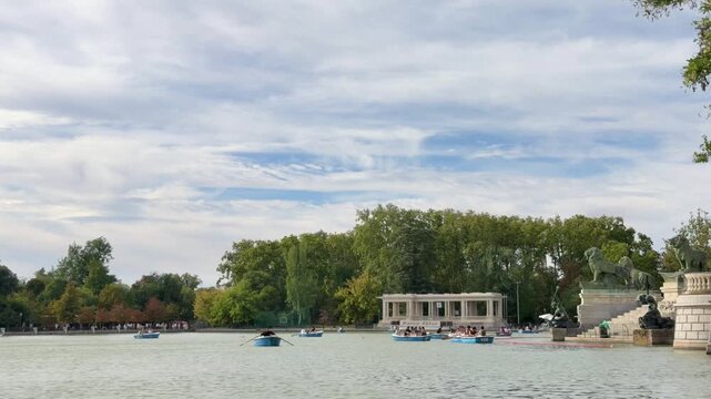 People enjoying a sunny day rowing boats on the Grand Pond in Retiro Park, with the Monument to Alfonso XII colonnade in the background, a popular tourist attraction in Madrid, Spain