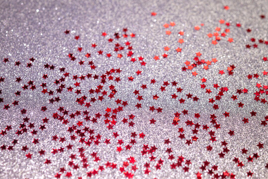 Festive red star confetti scattered across sparkling silver glitter background, creating a glamorous celebration texture for Christmas, New Year, party, holiday, birthday and decorative designs