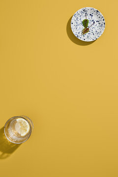 Yellow food background with clear lemon water and veined green leaves on a speckled plate for menu layout
