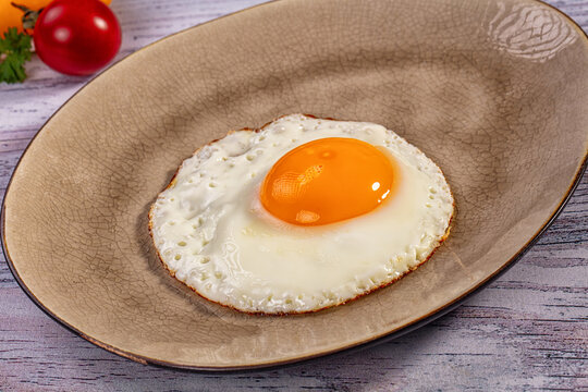 Cracked ceramic plate holding sunny side up egg with runny yolk and crisp edges, breakfast food