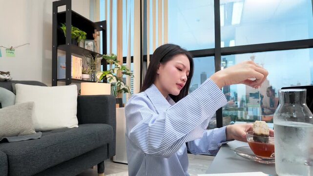 Asian Woman Dipping Tea Bag in Cup Working From Home