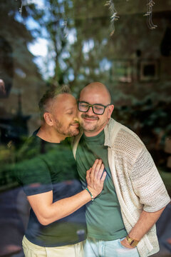 Two men standing with arms around each other by the living room window