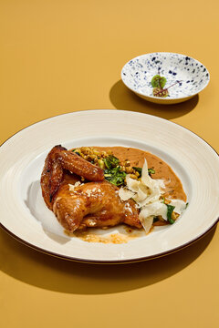 Roasted poussin with glazed brown skin, corn and curled cheese shavings on a yellow background for menu and recipe
