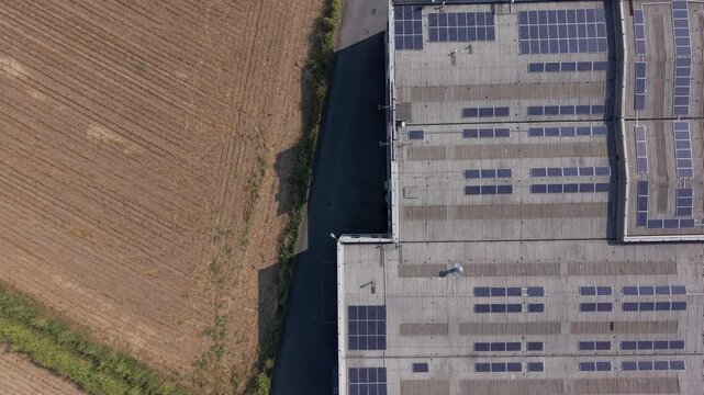 Top-down aerial view of a production facility roof covered with solar panels beside an open agricultural field in Italy