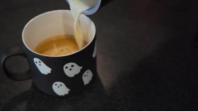 Oat milk is poured into coffee in a Halloween ghost mug, combining seasonal lifestyle imagery with plant based, vegan and dairy free coffee content.
