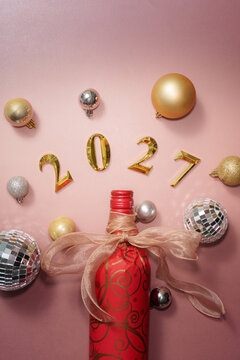 Happy New Year 2027 party concept with decorated wine bottle and disco balls on pink background