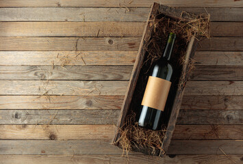 Obraz premium Bottle of red wine with empty label in an antique wooden box with hay.